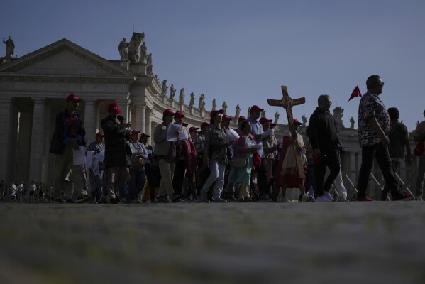 Pilgrims carrying a cross make their way to the Holy Door in St. Peter's Square at the Vatican after Cardinal Camerlengo Kevin Joseph Farrell announced the death of Pope Francis, Monday, April 21, 2025. (AP Photo/Alessandra Tarantino)