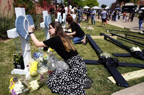 In this May 8, 2023, photo, Jennifer Seeley leaves a message on a cross that has the name of security guard Christian LaCour, written on it at a makeshift memorial in Allen, Texas. Jennifer Seeley was glued to her phone, safe at home but terrified nonetheless. There was an active shooter at the Texas mall where she works as an assistant store manager. And she was searching desperately for information, praying. Was the gunman dead? Were her coworkers dead? What was happening? (AP Photo/Tony Gutierrez, file)