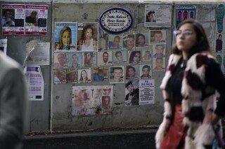 FILE - A woman passes in front of photographs of missing persons in front of the Attorney General's office in Mexico City, Dec. 6, 2023. The Mexican government announced Dec. 14, 2023 that its controversial effort to look for people falsely listed as missing has turned up thousands of individuals who had returned to their homes but not notified the authorities. (AP Photo/Eduardo Verdugo, Fille)