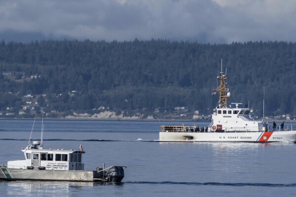 FILE - A U.S. Coast Guard boat and Kitsap, Wash., County Sheriff's Office boat search the area near Freeland, Wash., on Whidbey Island north of Seattle, Monday, Sept. 5, 2022. Representatives for all but one of the nine passengers killed in a seaplane crash near Washington state's Whidbey Island are suing the flight’s charter operator and aircraft manufacturer, saying the companies are responsible for the victims’ deaths. The three lawsuits, filed Tuesday, Aug. 22, 2023 in King County Superior Court, say the companies are responsible for the victims’ deaths, The Seattle Times reported. (AP Photo/Stephen Brashear, File)