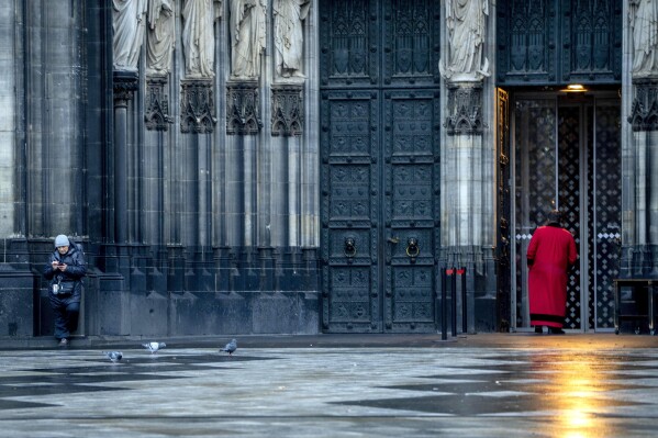 FILE - A cathedral door keeper and a woman wait in front of the Cathedral in Cologne, Germany, on Nov. 30, 2022. A court on Tuesday, June 13, 2023, ordered a German diocese to pay 300,000 euros ($323,000) in compensation to a man who was repeatedly abused by a Catholic priest in the 1970s, a ruling that a victims' association said was the first of its kind in Germany. The state court in Cologne ruled in a case in which the plaintiff, a man now aged 62 who was abused more than 300 times by a priest, had sought 750,000 euros from the Cologne archdiocese, German news agency dpa reported. (AP Photo/Michael Probst)