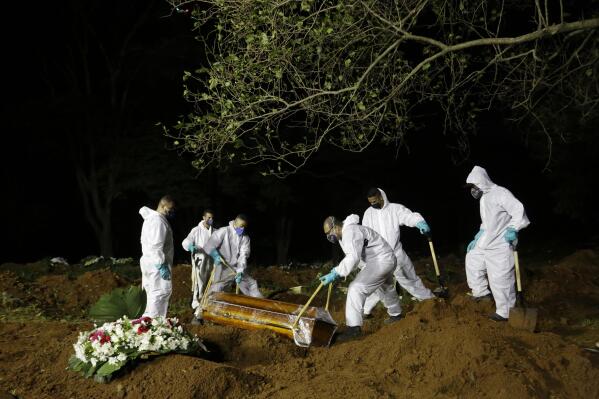 FILE - In this March 31, 2021 file photo, cemetery workers work hours past sundown, as they lower the coffin that contain the remains of a COVID-19 victim into a freshly dug grave at the Vila Formosa cemetery in Sao Paulo, Brazil. Nighttime burials at Vila Formosa and three other cemeteries in Sao Paulo were suspended Wednesday, April 28, after two weeks of declining deaths. (AP Photo/Nelson Antoine, File)