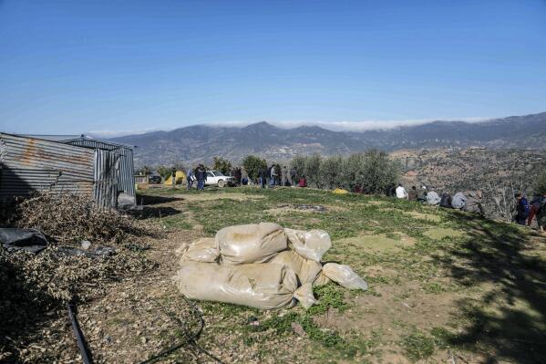 Bags of harvested cannabis left to dry in the sun as mourners gather around a hill at the funeral of five year old Rayan after his body was retrieved from a deep well, in the village of Ighran in Morocco's Chefchaouen province, Monday, Feb. 7, 2022. The death of a 5-year-old boy trapped for days in the dark depths of a well symbolizes for many villagers a curse that haunts their remote mountainous region in northern Morocco. Rif is dirt poor, neglected and dependent on its illegal cannabis crop to survive. Rayan’s plight riveted world attention during five days of vain efforts to save him. The well that swallowed Rayan was dug by his father in a vain bid to forage for water so he could grow cannabis, or marijuana. Such wells dot the rugged Rif region. (AP Photo/Mosa'ab Elshamy)