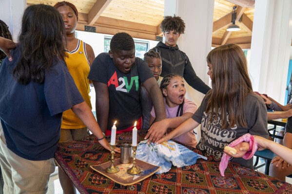 Judah, 10, of Vermont, center, and Kallie House, 12, of Sugar Land, Texas, right, react after the prayer over the challah bread is recited during Shabbat at Camp Be'chol Lashon, a sleepaway camp for Jewish children of color, Friday, July 28, 2023, in Petaluma, Calif., at Walker Creek Ranch. Standing behind them is Josiah Spencer, 15, who is the son of the camp's director. (AP Photo/Jacquelyn Martin)