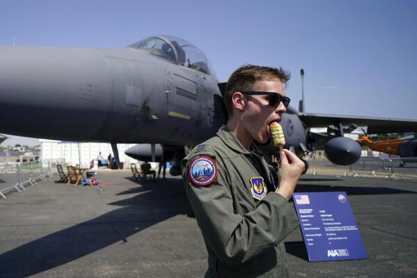 FILE - A member of the military personnel eats an ice cream as he stands past an F15E Strike Eagle fighter jet, on display at the Farnborough Air Show fair in Farnborough, England, Tuesday, July 19, 2022. The future for fighter pilots was on display at the Farnborough International Airshow near London, one of the world’s biggest aviation, defense and aerospace expos. New technologies take on a bigger role in the cockpit, redefining what it means to be a ''Top Gun''. (AP Photo/Alberto Pezzali, File)