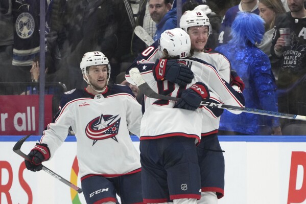 Columbus Blue Jackets center Kent Johnson (91) celebrates his overtime goal against the Toronto Maple Leafs with Dmitri Voronkov (10) and Justin Danforth (17) in an NHL hockey game Thursday, Dec. 14, 2023, in Toronto. (Nathan Denette/The Canadian Press via AP)