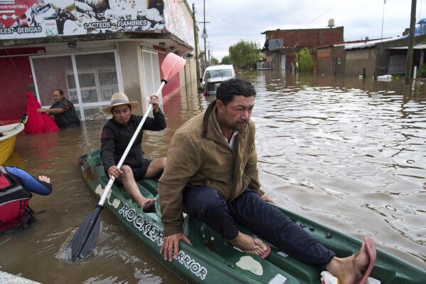 A man paddles a neighbor through flooded streets following heavy rains in Campana, Argentina, Saturday, May 17, 2025. (AP Photo/Rodrigo Abd)