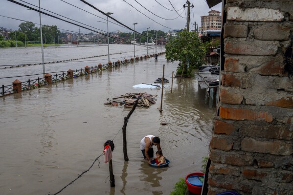 A man puts his child on a plastic vessel to play in flood waters of the Bagmati river following heavy monsoon rains in Kathmandu, Nepal, Tuesday, Aug. 8, 2023. (AP Photo/Niranjan Shrestha)