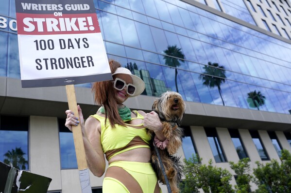 Phoebe Price carries her dog Arnold along with a sign on a picket line outside Netflix studios on Wednesday, Aug. 9, 2023, in Los Angeles. The Hollywood writers strike reached the 100-day mark today as the U.S. film and television industries remain paralyzed by dual actors and screenwriters strikes. (AP Photo/Chris Pizzello)