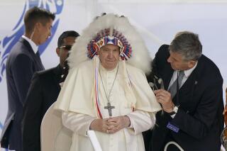 FILE - Pope Francis dons a headdress that was gifted to him during a visit with Indigenous peoples at Maskwaci, the former Ermineskin Residential School, Monday, July 25, 2022, in Maskwacis, Alberta. The Vatican Museums officially reopened its African and American ethnographic collections Thursday, March 16, 2023, by showcasing intricately restored Rwandan raffia screens that were sent by Catholic missionaries to the Vatican for a 1925 exhibit. (AP Photo/Eric Gay, File)