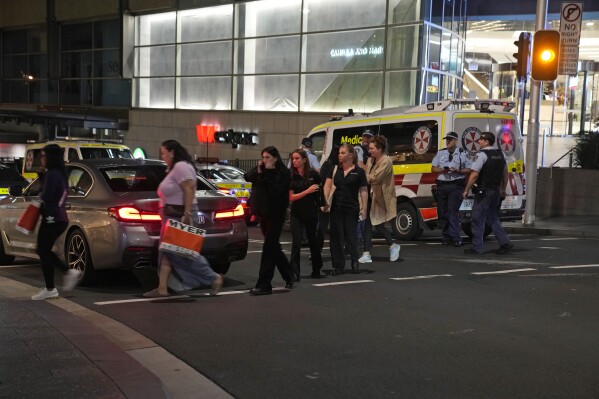 People are led out from the Westfield Shopping Centre where multiple people were stabbed in Sydney, Saturday, April 13, 2024. A man stabbed six people to death at the busy Sydney shopping center Saturday before he was fatally shot, police said. Multiple people, including a small child, were also injured in the attack. (AP Photo/Rick Rycroft)