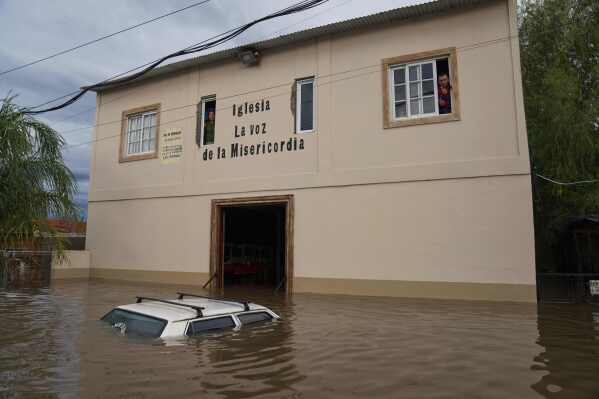 A vehicle sits partially submerged in floodwaters as residents look out from the windows of a church, following heavy rains in Campana, Argentina, Saturday, May 17, 2025. (AP Photo/Rodrigo Abd)