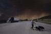 A person takes his dogs out for a quick break under billowing wildfire smoke off Highway 97 north of Buckinghorse River, British Columbia, May 30, 2025. (Nasuna Stuart-Ulin/The Canadian Press via AP, File)