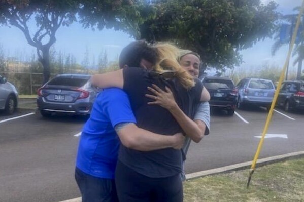 This Aug. 9, 2023 photo taken by his stepfather Mike Eilers and provided by Mike Cicchino shows Mike Cicchino, left, and his wife Andreza, right, hugs Mike's mother Susan Ramos as they were reunited at shelter in Maui, Hawaii. (Mike Cicchino via AP)