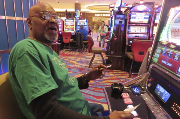 Steve Mitchell, of Wilmington, Del., smokes while he plays a slot machine at the Hard Rock casino in Atlantic City, N.J., on Feb. 2, 2024. Competing bills in the New Jersey Legislature in February 2024 would either ban smoking outright in Atlantic City's nine casinos or allow it to continue with additional restrictions. (AP Photo/Wayne Parry)
