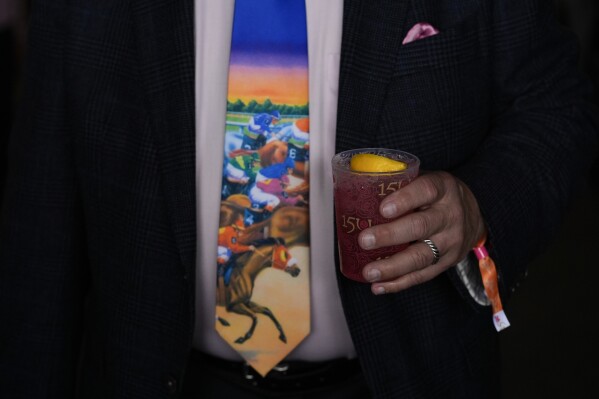 Horse racing fans walk through the grounds of Churchill Downs with drinks in hand before the 150th running of the Kentucky Oaks on Friday, May 3, 2024 in Louisville, Kentucky (AP Photo/Charlie Riedel)