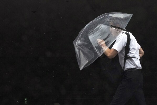 A man holds an umbrella against strong wind and rain as he walks on a street Friday, June 2, 2023, in Tokyo, as a tropical storm was approaching. (AP Photo/Eugene Hoshiko)