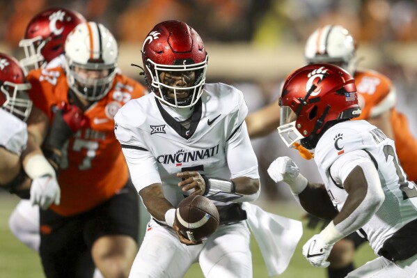 Cincinnati's Emory Jones, left, hands the ball off to Myles Montgomer during the first half of the team's NCAA college football game against Oklahoma State on Saturday, Oct. 28, 2023, in Stillwater, Okla. (AP Photo/Mitch Alcala)