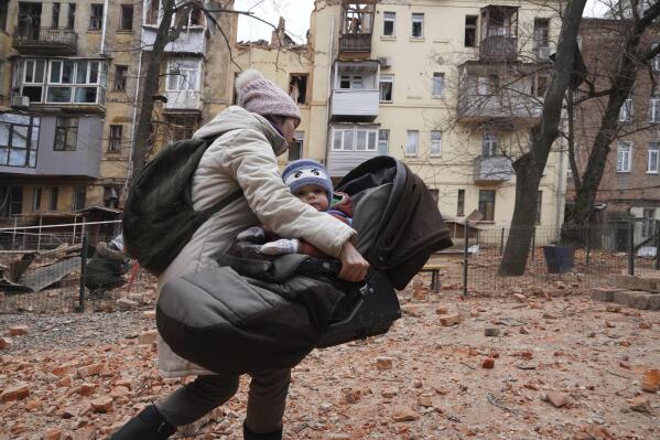 A woman carries her child as they evacuate from a residential building which was hit by a Russian rocket at the city center of Kharkiv, Ukraine, Monday, Jan. 30, 2023. Russian shelling killed at least five people and wounded 13 others during the previous 24 hours, Ukrainian authorities said Monday as the Kremlin’s and Kyiv’s forces remained locked in combat in eastern Ukraine. (AP Photo/Andrii Marienko)