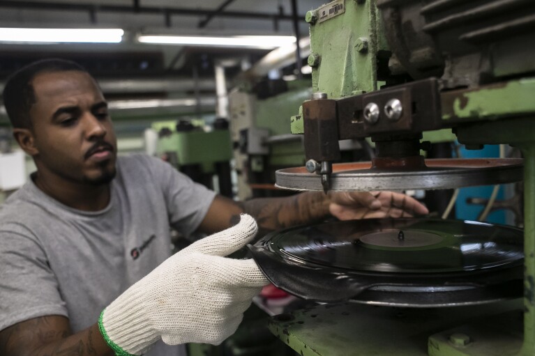 An operator trims a pressed record at the Polysom factory, in Belford Roxo, Brazil, Tuesday, April 16, 2024. In Brazil, vinyl records outsold CDs and DVDs for the first time last year. (AP Photo/Bruna Prado)