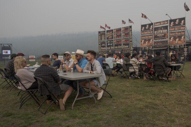 People eat barbecue at a festival despite heavy smoke from wildfires in Fort McMurray, Canada, on Saturday, Sep. 2, 2023. (AP Photo/Victor R. Caivano)