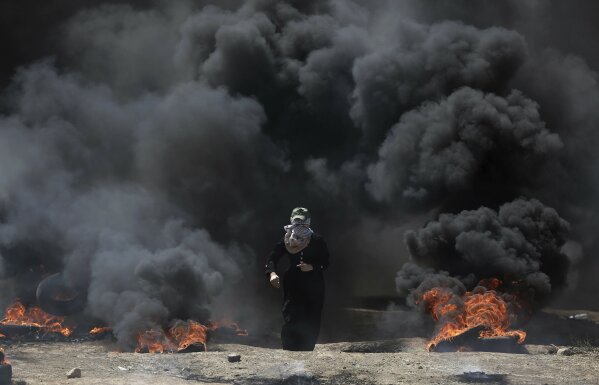 
              A Palestinian woman walks through black smoke from burning tires during a protest on the Gaza Strip's border with Israel, Monday, May 14, 2018. Thousands of Palestinians are protesting near Gaza's border with Israel, as Israel prepared for the festive inauguration of a new U.S. Embassy in contested Jerusalem. (AP Photo/Khalil Hamra)
            
