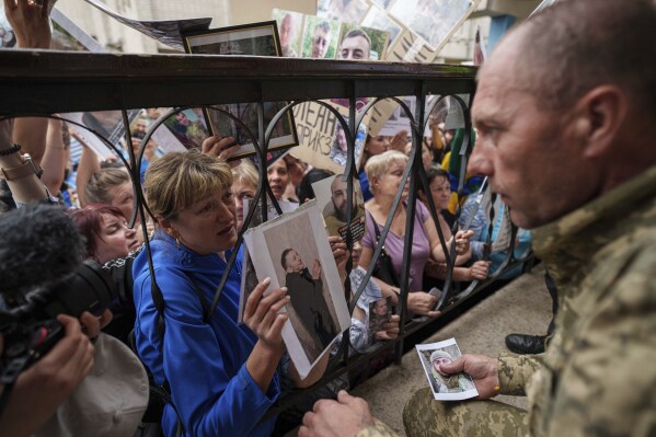 People show photos of their missed relatives to Ukrainian soldiers during a POWs exchange between Russia and Ukraine, in Chernyhiv region, Ukraine, Saturday, May 24, 2025. (AP Photo/Evgeniy Maloletka)