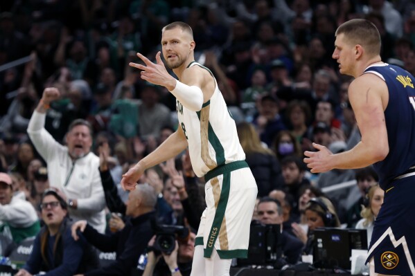 Boston Celtics' Kristaps Porzingis (8) reacts in front of Denver Nuggets' Nikola Jokic (15) after making a 3-pointer during the first half of an NBA basketball game Friday, Jan 19, 2024, in Boston. (AP Photo/Michael Dwyer)