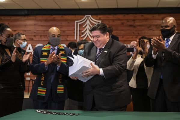 FILE - Flanked by lawmakers and supporters, Gov. J.B. Pritzker picks up the nearly 800-page criminal justice reform bill after signing it into law during a ceremony at Chicago State University in Chicago, Monday, Feb. 22, 2021. The wide-ranging criminal justice overhaul, spurred by police-involved deaths of George Floyd and others, will be implemented, Jan. 1, 2022. It is a first-ever statewide certification and decertification process for police officers. (Ashlee Rezin Garcia/Chicago Sun-Times via AP, File)