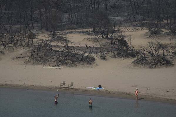 People play with a ball in front of a burnt forest at a beach, near Gennadi village, on the Aegean Sea island of Rhodes, southeastern Greece, on Thursday, July 27, 2023. The wildfires have raged across parts of the country during three successive Mediterranean heat waves over two weeks, leaving five people dead. (AP Photo/Petros Giannakouris)