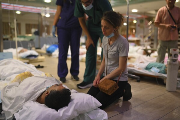 A woman sits next to a patient on the floor of a ferry boat after health authorities partially evacuated a hospital in Alexandroupolis, in the northeastern Evros region, Greece, early Tuesday, Aug. 22, 2023. (e-evros.gr via AP)