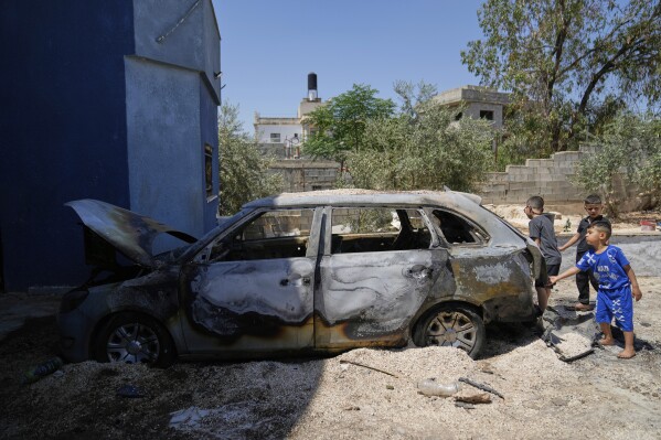 Palestinian boys play by their family's vehicle, which was burnt during an overnight attack by Israeli settlers and left several burnt vehicles and damaged homes, residents said, in the West Bank village of Bruqin, near Salfit, Friday, May 23, 2025. (AP Photo/Nasser Nasser)
