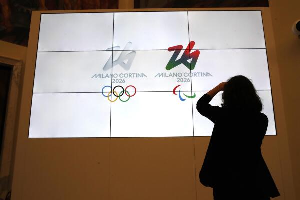 FILE - The logo of 2026 Milan-Cortina Olympics and Paralympics, right, are unveiled to the journalists at a press conference in Rome, March 30, 2021. Another expensive venue for the 2026 Milan-Cortina Winter Olympics has been approved, with a 50 million euro ($50 million) project slated to place a roof over the outdoor speedkating oval in Baselga di Pine. The Milan-Cortina organizing committee said Tuesday, Nov. 8, 2022 that it couldn’t comment on "a choice made by Baselga,” but noted that speedskating was slated for Baselga in the bid dossier and that the International Skating Union prefers an indoor oval.(AP Photo/Alessandra Tarantino, file)