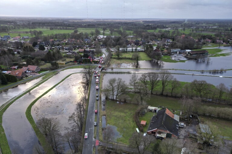 Firefighters are seen at center as they try to secure the area with sandbags from floodwaters from the Burlage-Langholter Tief, a tributary of the Leda, after it overflowed, in Langholt, Germany, Tuesday, Dec. 26, 2023. Firefighters and volunteers labored to reinforce dikes against rising floodwaters in northern and eastern Germany as heavy rains falling on already soaked ground pushed rivers and streams over their banks and forced several towns to evacuate residents. (Lars Penning/dpa via AP)