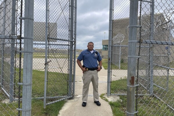 Maj. Albin Narvaez stands in the gated entryway to the prison yard at the Fulton Reception and Diagnostic Center, Thursday, July 13, 2023, in Fulton, Missouri. Narvaez, who is chief of custody at the prison, said applications for correctional officers have increased since the state implemented a pay raise this spring. (AP Photo/David A. Lieb)