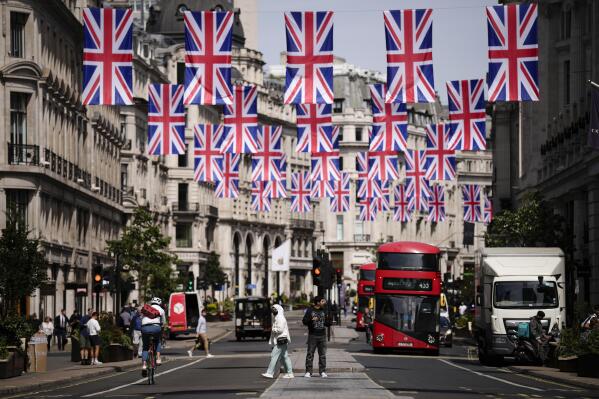 FILE - People cross the Regent Street shopping district with Union flags hanging over it to mark the upcoming Platinum Jubilee of the 70 year reign of Britain's Queen Elizabeth II, in London, Wednesday, May 18, 2022. Britain’s economy showed unexpectedly strong growth in May, with an expansion of 0.5% in domestic product, reported The Office for National Statistics. The Confederation of British Industries cautioned that the figures can be volatile, with May data skewed by an extra public holiday marking Queen Elizabeth II's 70 years on the throne. (AP Photo/Matt Dunham, File)