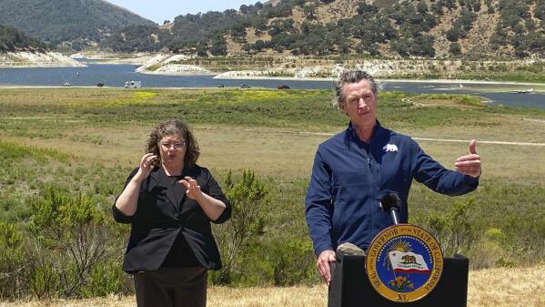Gov. Gavin Newsom and interpreter Julia Townsend stand at the edge of a diminished Lopez Lake near Arroyo Grande, Calif., Thursday, July 8, 2021. Newsom has asked people and businesses in the nation's most populous state to voluntarily cut how much water they use by 15% amid a drought. Newsom's request is not an order. But it demonstrates the growing challenges of a drought that will only worsen throughout the summer and fall and is tied to recent heat waves. (David Middlecamp/The Tribune (of San Luis Obispo) via AP)