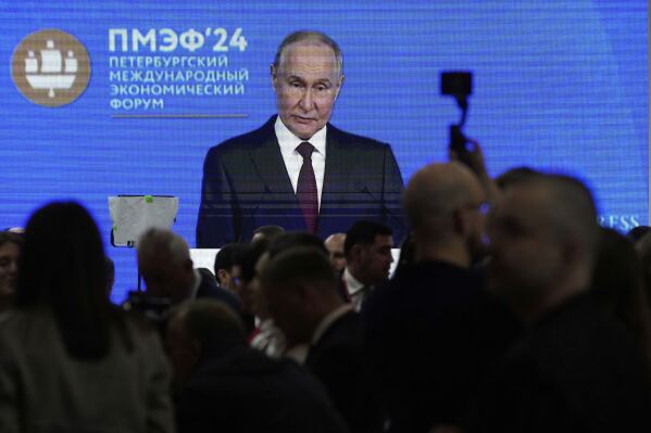 Guests and participants walk in front of a TV screen showing Russian President Vladimir Putin on the sidelines of the St. Petersburg International Economic Forum in St. Petersburg, Russia, Wednesday, June 18, 2025. (AP Photo/Dmitri Lovetsky)