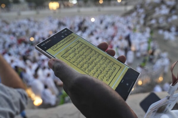 A Muslim pilgrim uses a mobile phone to read chapters from the holy Quran atop the rocky hill known as the Mountain of Mercy, on the Plain of Arafat, during the annual Hajj pilgrimage near the holy city of Mecca, Saudi Arabia, Thursday, June 5, 2025. (AP Photo/Amr Nabil)