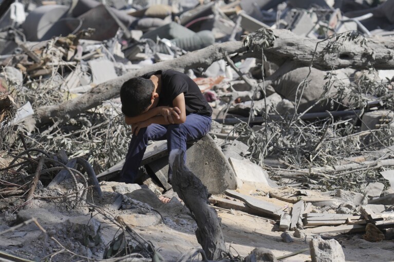A Palestinian boy sits on the rubble of the building destroyed in an Israeli airstrike in Bureij refugee camp Gaza Strip, Wednesday, Oct. 18, 2023. (AP Photo/Hatem Moussa)