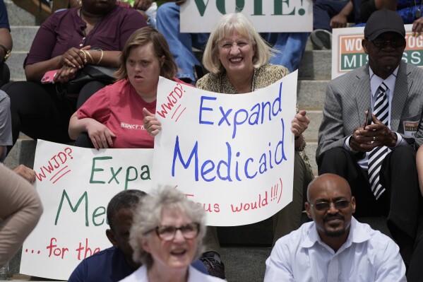 Linda Breazeale, right, and her daughter Debra Ann Breazeale, hold homemade support signs at the Mississippi Medicaid Expansion Rally at the Mississippi State Capitol in Jackson, Tuesday, April 16, 2024. (AP Photo/Rogelio V. Solis)