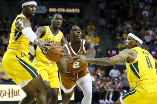 Texas guard Marcus Carr, center, turns over the ball as he is defended by Baylor forward Flo Thamba, left and Baylor guard James Akinjo, right during the first half of an NCAA college basketball game on Saturday, Feb. 12, 2022, in Waco, Texas. (AP Photo/Ray Carlin)