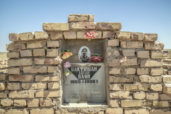 Flowers are visible on a woman's gravesite near the dried-up Aral Sea outside Muynak, Uzbekistan, Monday, June 26, 2023. (AP Photo/Ebrahim Noroozi)