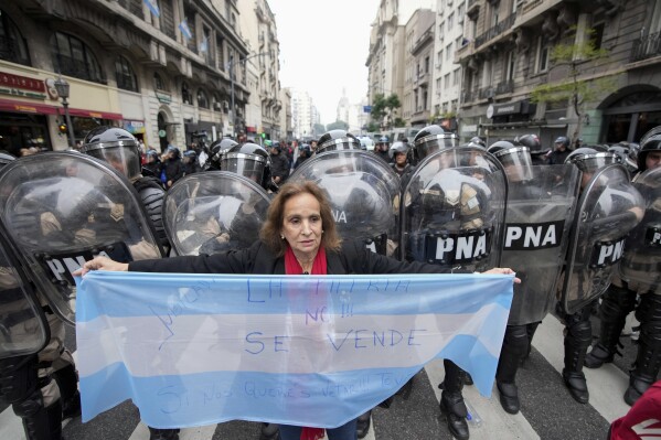 An anti-government protester holds an Argentine flag by police near Congress where lawmakers debate a reform bill promoted by Argentine President Javier Milei in Buenos Aires, Argentina, Wednesday, June 12, 2024. (AP Photo/Natacha Pisarenko)