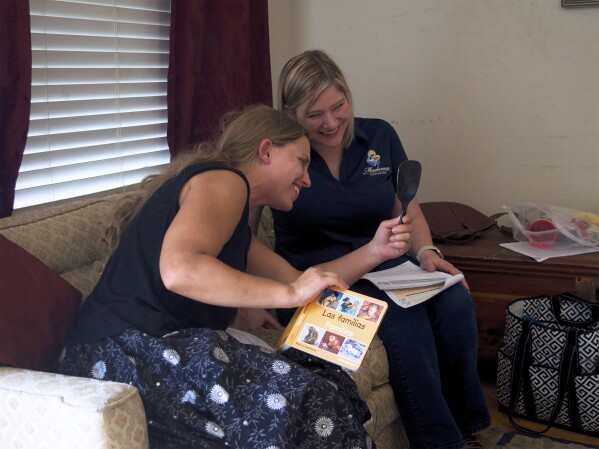 Home visitor Amanda Pedlar and parent Bridget Collins check their smiles in a mirror, illustrating what someone might look like when they are happy, during a role-playing activity on March 4, 2024, in San Antonio, Texas. Home visit programs have provided a lifeline for families, especially those for whom access to qualify early education is scarce or out of reach financially. (Emily Tate Sullivan/EdSurge via AP)