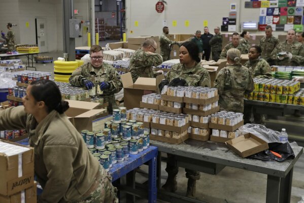 FILE - In this March 24, 2020, file photo, members of The Ohio National Guard assist in repackaging emergency food boxes for food distribution at the Cleveland Food Bank in Cleveland. The use of National Guard units around the country to help with the response to the coronavirus pandemic is prompting rumors of a national lockdown or even martial law. Guard units are now helping to transport medical supplies, distribute food and even help direct traffic at drive-through testing sites. (AP Photo/Tony Dejak, File)