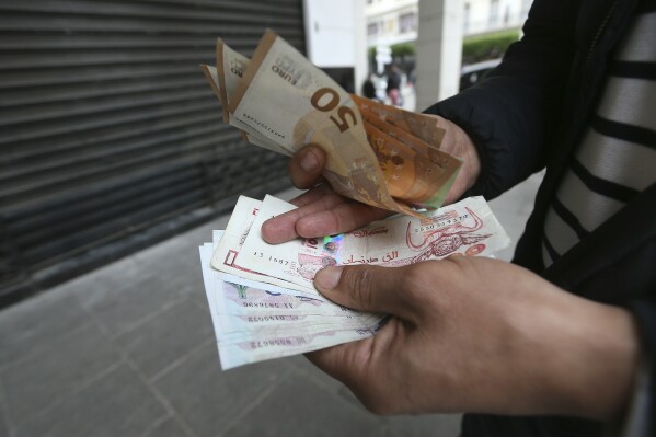 A man holds Algerian and European, top, bank notes Friday, Feb. 9, 2024 in Algiers. In Algeria, people have long relied on foreign currencies to buy imported items in short supply or finance their children's educations abroad. But the value of the Algerian dinar has recently swung wildly on the country's black market as its value has plummeted compared to euros, pounds and dollars. The oil-rich country's large black market for foreign currency is among the signs of its economic woes. (AP Photo/Anis Belghoul)