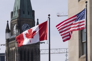 FILE - The Canadian and U.S. flags are displayed on lamp posts in the downtown area, March 22, 2023, near Parliament Hill in Ottawa, Ontario. On Tuesday, Aug. 29, Canada updated its travel advisory to the U.S., warning members of the LGBTQ+ community that some American states have enacted laws that may affect them. (Adrian Wyld/The Canadian Press via AP, File)