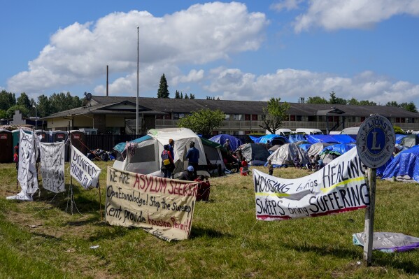 Signs line the front of an encampment of asylum-seekers mostly from Venezuela, Congo and Angola next to an unused motel owned by the county, Wednesday, June 5, 2024, in Kent, Washington. The group of about 240 asylum-seekers is asking to use the motel as temporary housing while they look for jobs and longer-term accommodations. (AP Photo/Lindsey Wasson)