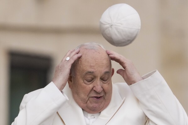 FILE - Pope Francis tries to catch his cap as wind blew it away while arriving for his weekly general audience in the St. Peter's Square at the Vatican, Wednesday, March 13, 2024. (AP Photo/Andrew Medichini, File)